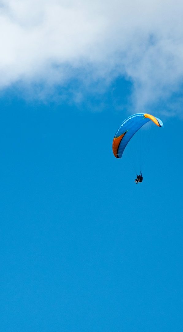 Un parapente coloré plane dans un ciel bleu avec quelques nuages.