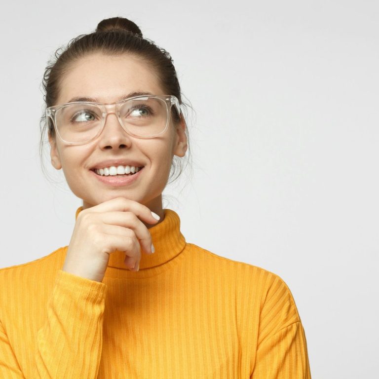 postures Femme aux cheveux courts et roux, portant des lunettes, regard pensif, doigt sur le menton.
